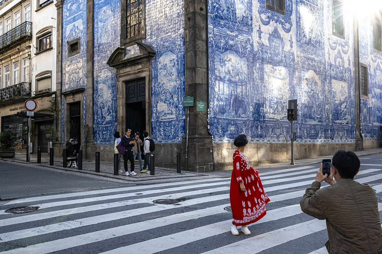 Mulher de vestido vermelho atravessa passadeira em frente à Capela das Almas, Porto