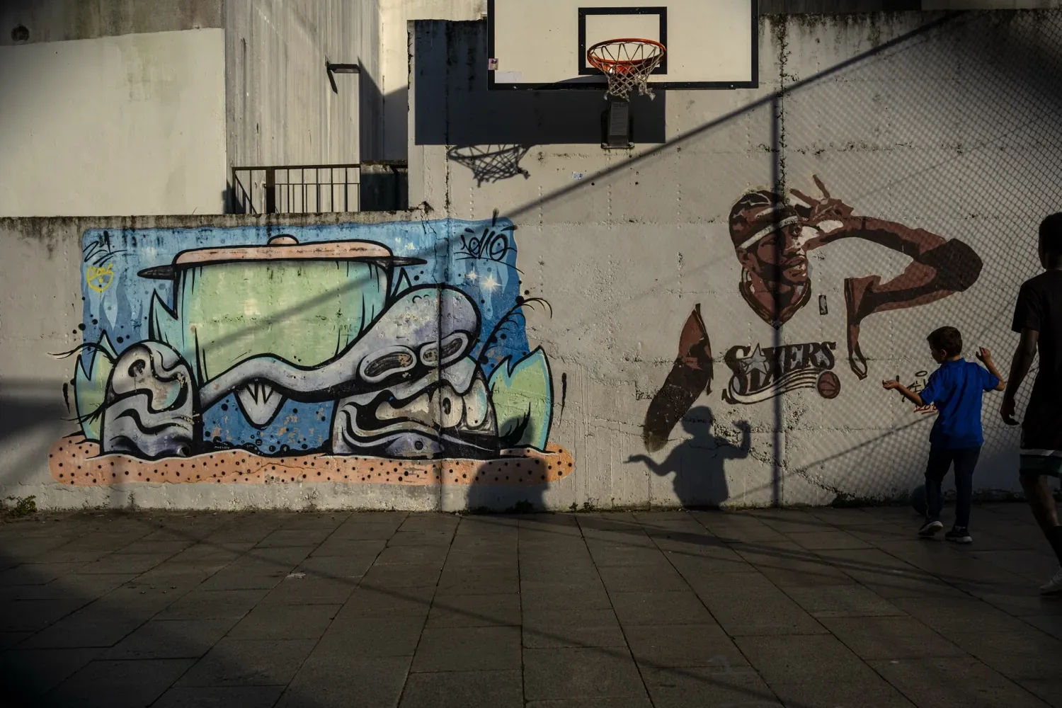 Crianças num campo de basquetebol urbano com graffiti e sombras ao fim do dia, Porto