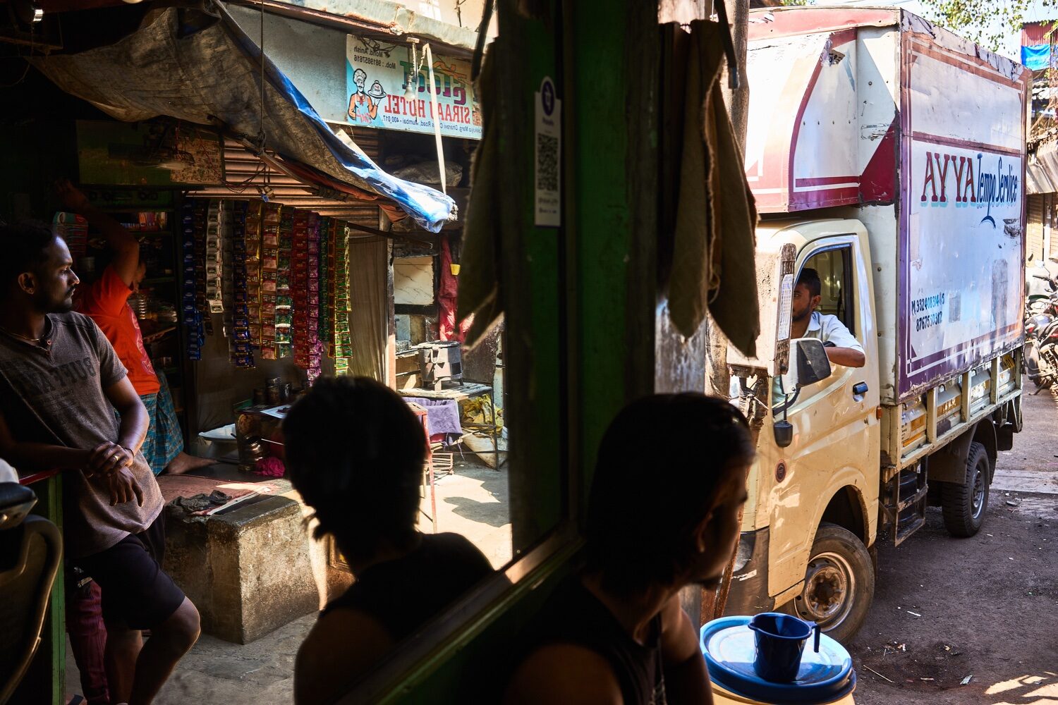 Cena de rua num mercado de Mumbai com camião de entrega e habitantes em frente a lojas